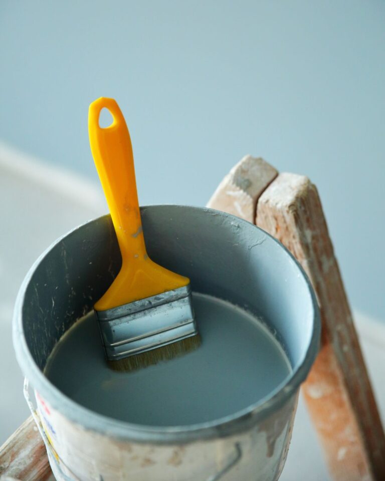 Paintbrush resting in a bucket of grey paint